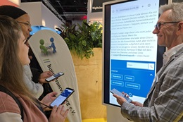  Für die Smart Country Convention 2024 wurden die Standbesucher eingeladen mit ihrem eigenen Personalausweis und ihrem eigenen Smartphone das Online-Ausweisen selbst zu erleben. An einem Riesen-Smartphone wurde die passende Anleitung gegeben. (Foto: buergerservice.org e.V.)